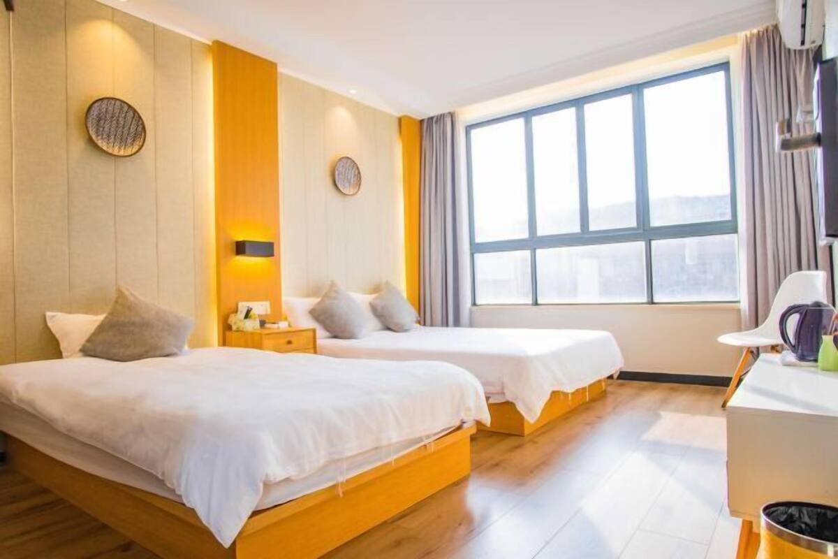 A hotel room with two beds, a desk, and a large window.
