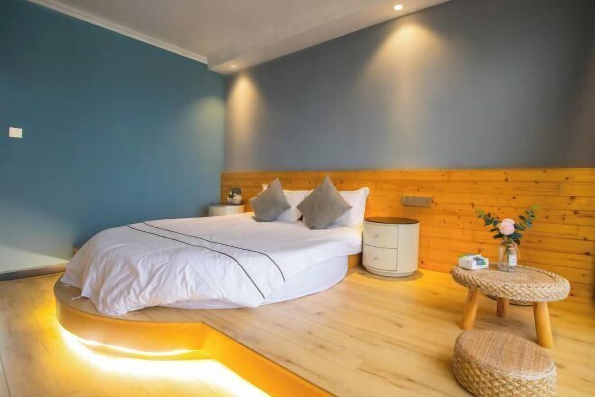 A bedroom with a bed, bedside table, nightstand, and a small round table with a vase.
