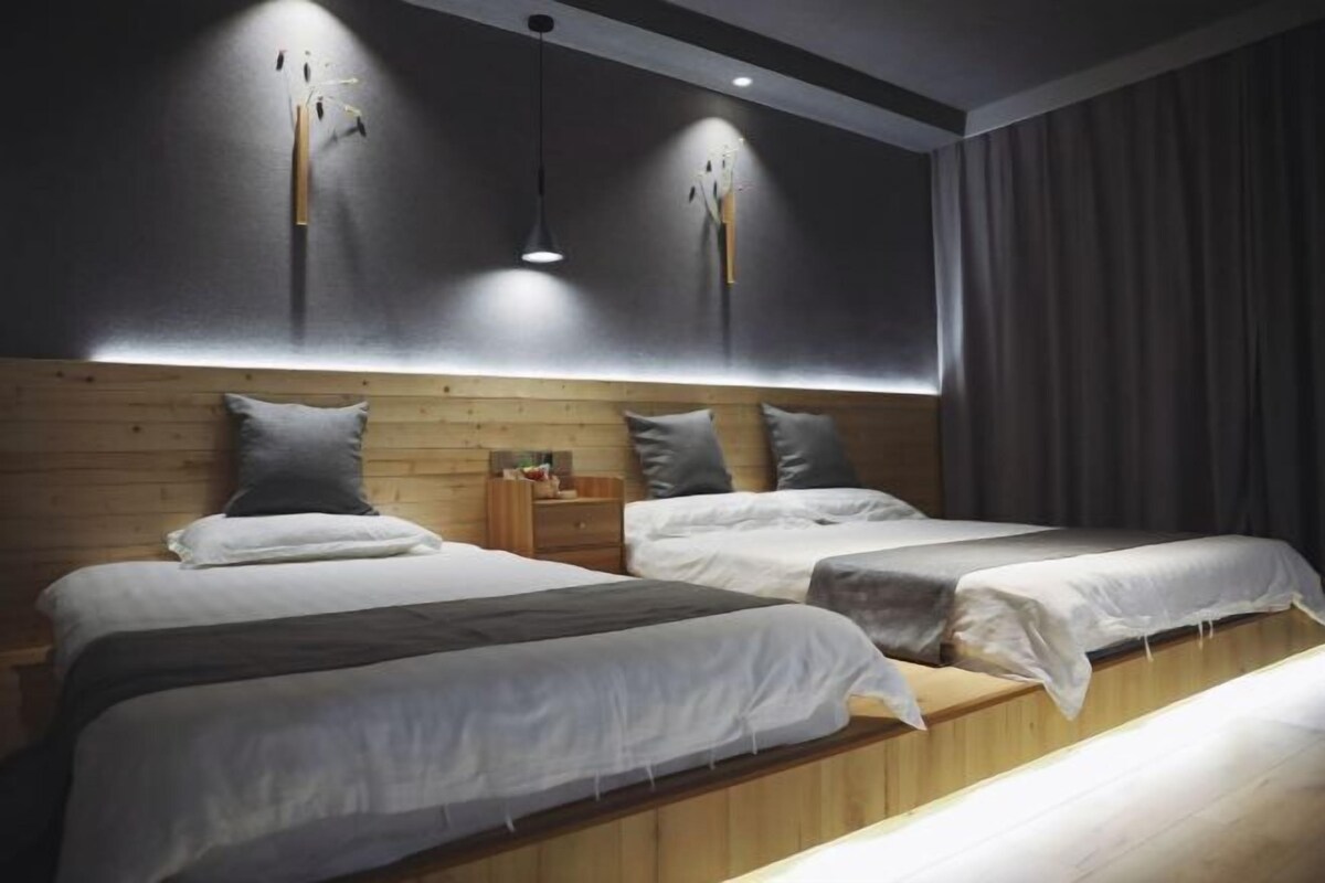 A modern hotel room with two beds, wooden headboard, pendant lighting, and a large window with curtains.