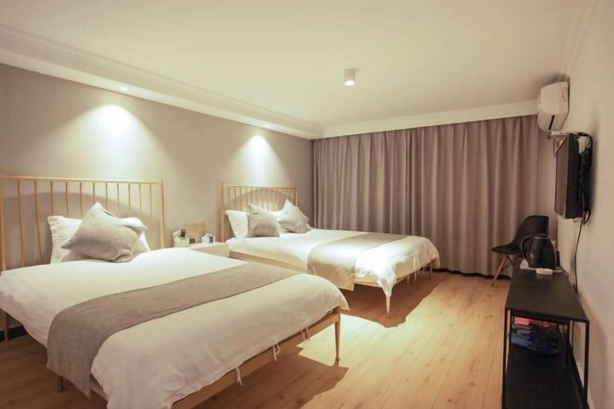 A hotel room with two beds, a desk, a chair, and a wall-mounted TV.