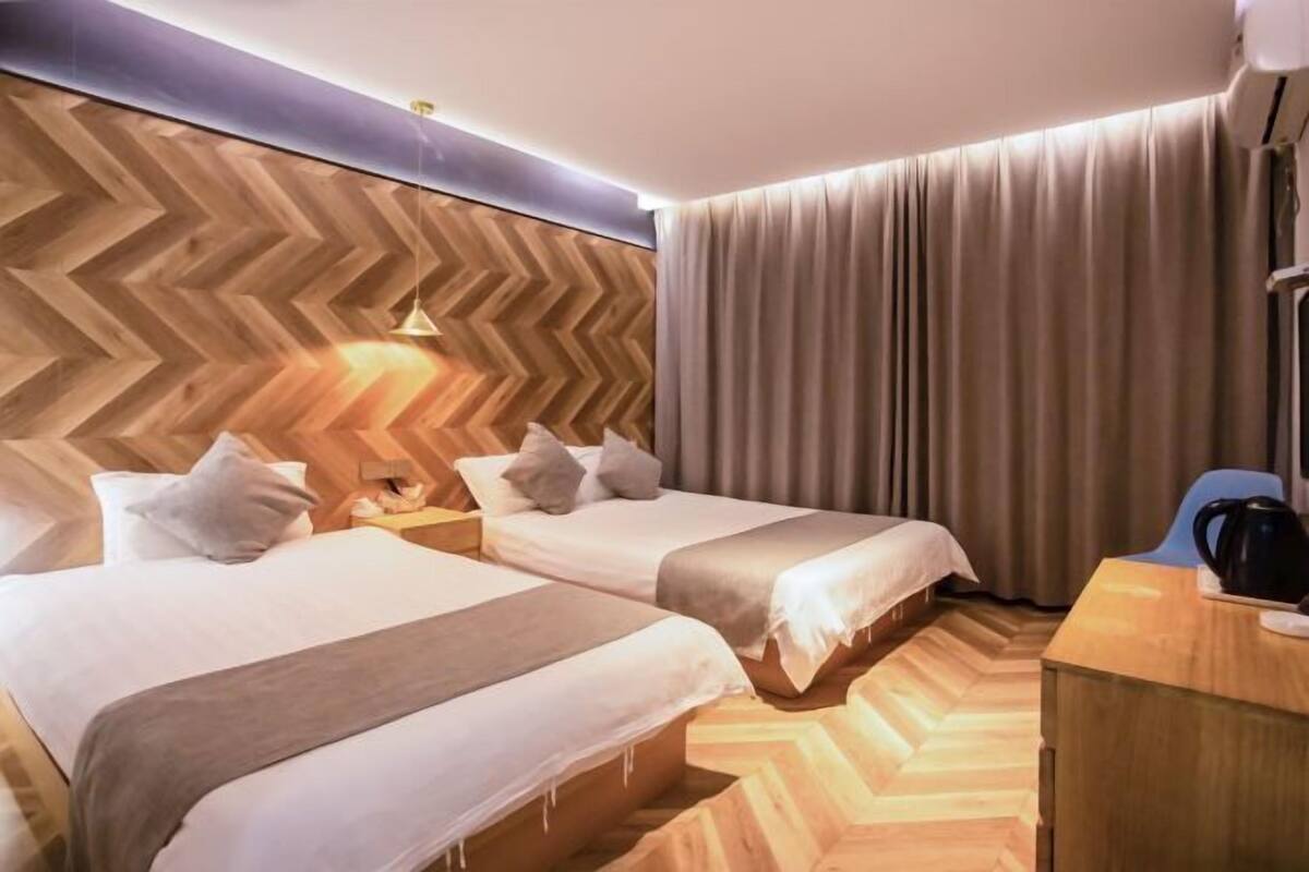 A hotel room with two beds, a wooden herringbone-patterned wall, a wooden desk, and a curtain.