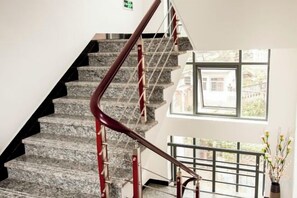 A staircase with a red handrail and metal balusters, leading to a landing with a window and a plant. - Shengsi Haiyi Lanting Homestay (Shengsi)