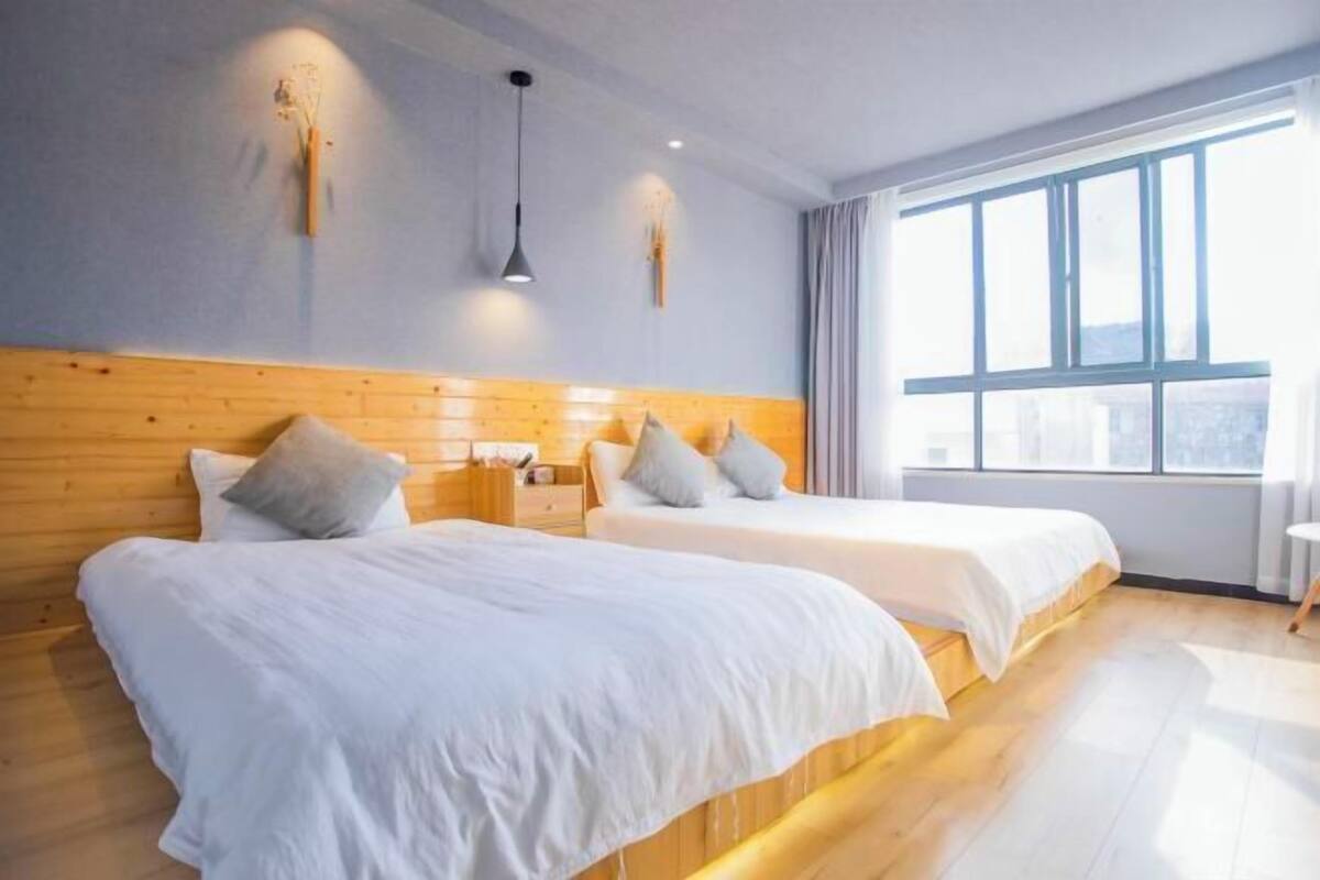 A hotel room with two beds, wooden headboard, bedside tables, and a large window.