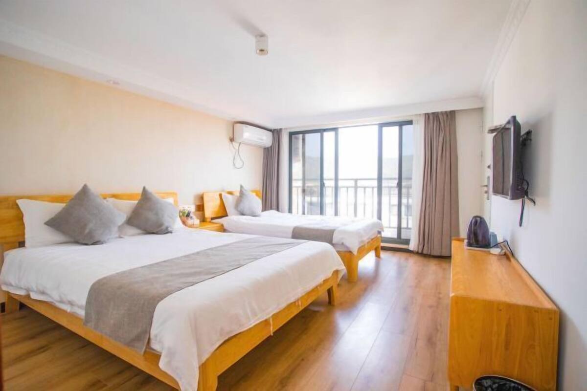A hotel room with two beds, a TV, a desk, and a large window.