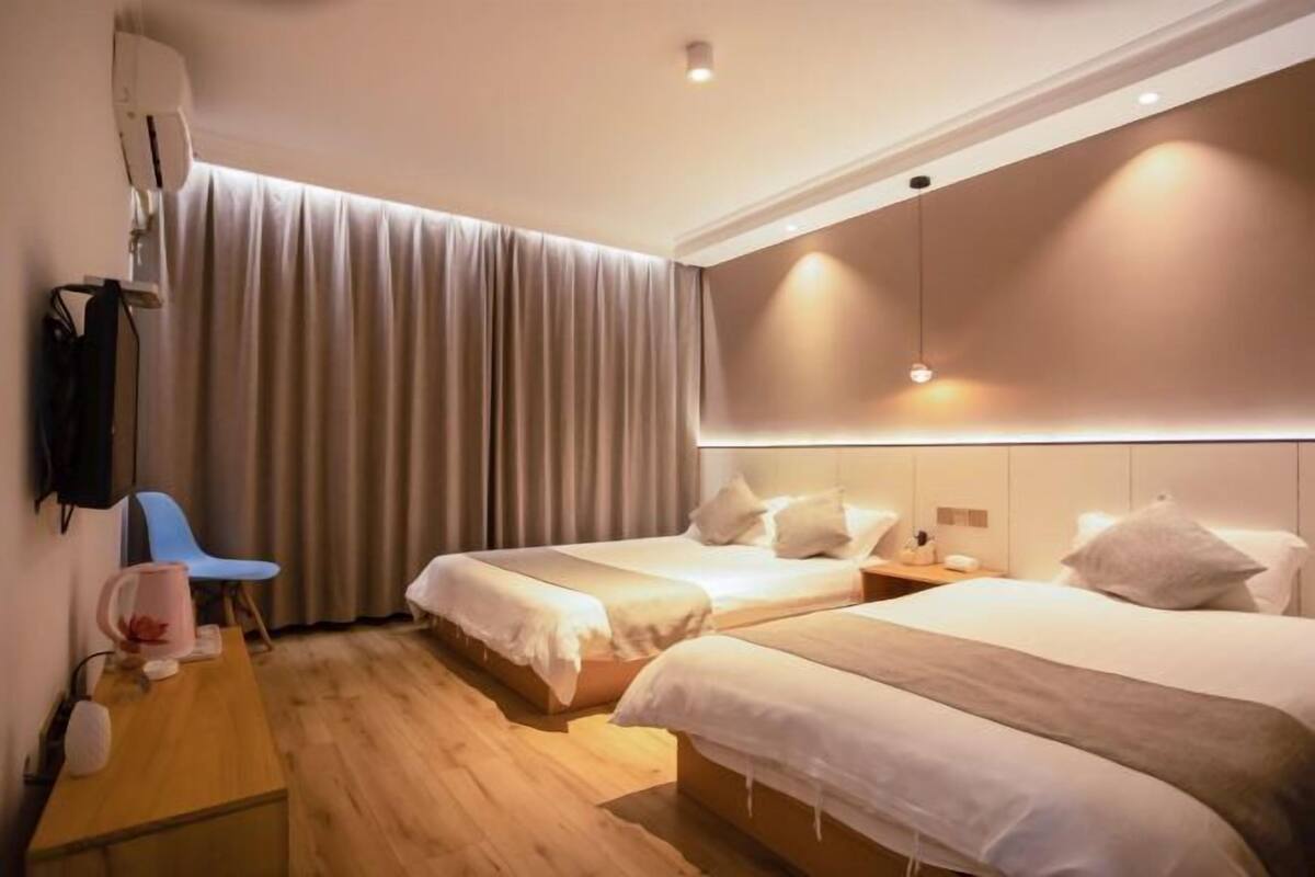 A hotel room with two beds, a desk, a chair, a TV, and a large window with curtains.