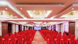 Une salle de conférence avec des rangées de chaises rouges et un grand écran à l’avant.