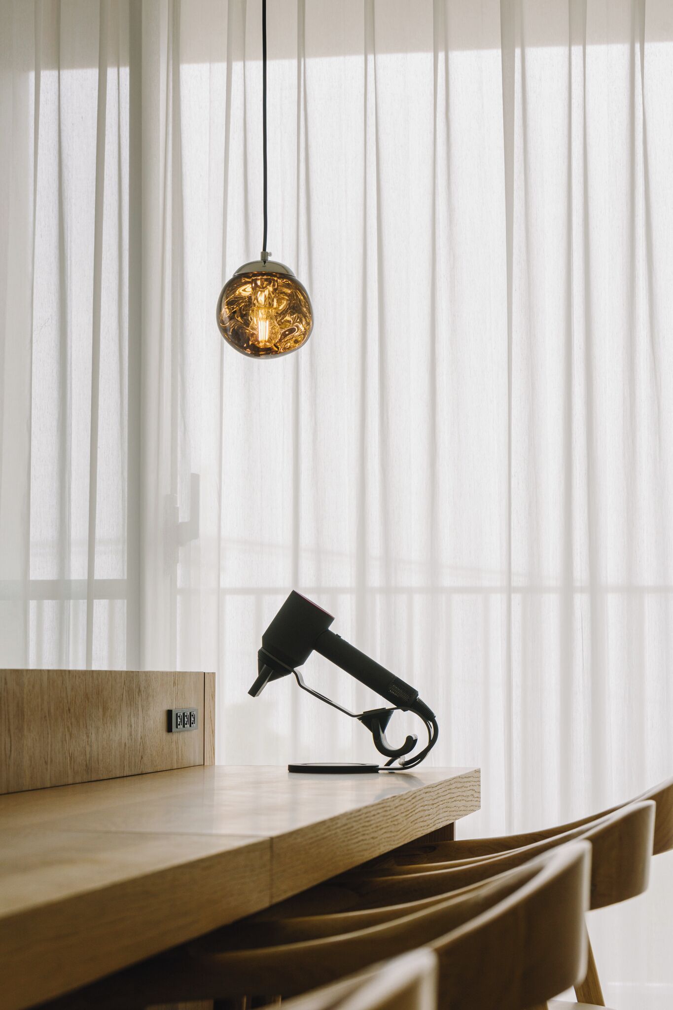 Een houten tafel met een zwarte lamp en een doosje met de tekst 'B&B', voor een achtergrond van lichte, witte gordijnen.