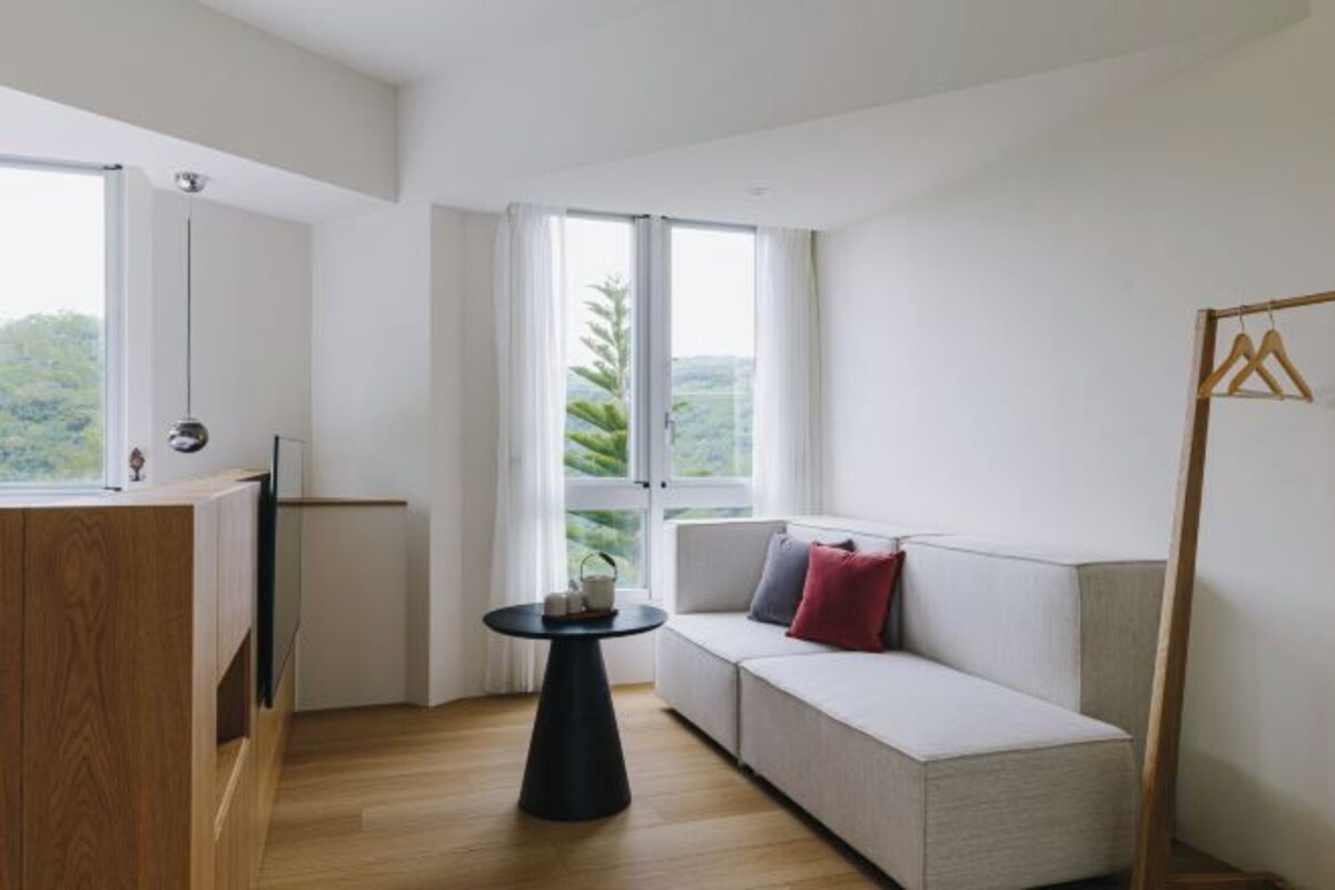 A modern living room with a wooden cabinet, a round black table, and a light-colored sofa with red and gray cushions.