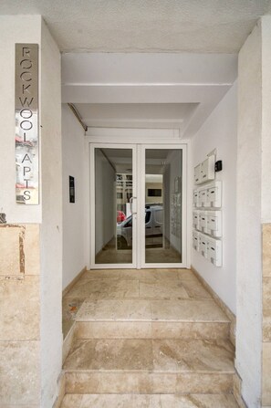 Enter a hallway leading to a room with a double door, featuring a tiled floor and a wall-mounted electrical panel.