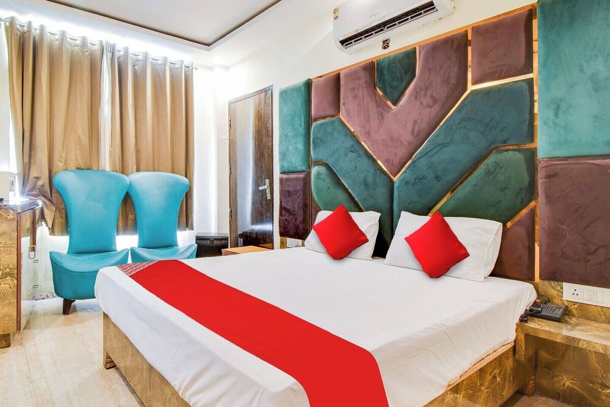A hotel room with a large bed, two blue chairs, a marble accent wall, and a modern design.