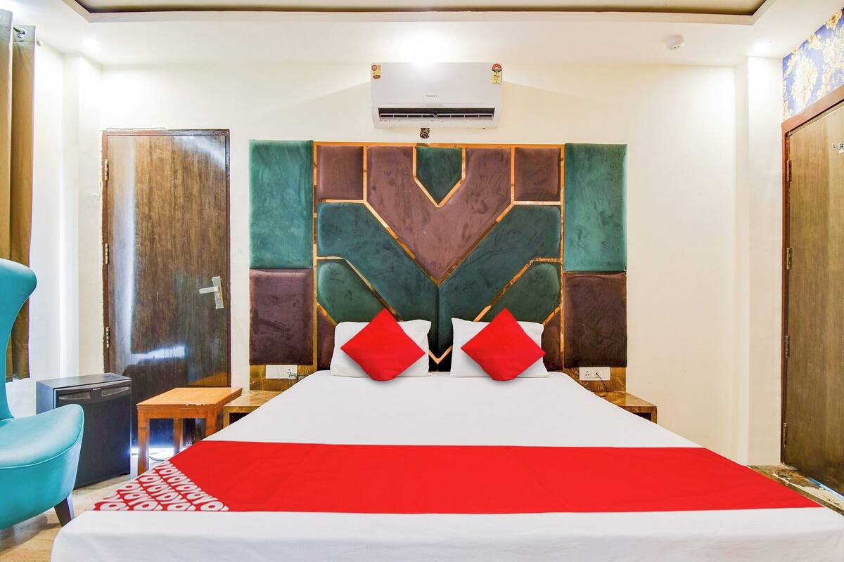 A hotel room with a bed, a desk, a chair, and an air conditioning unit.