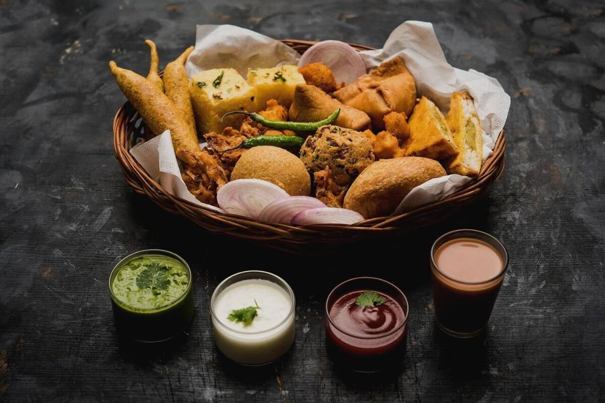 A basket of fried snacks and two types of chutneys on a dark surface.
