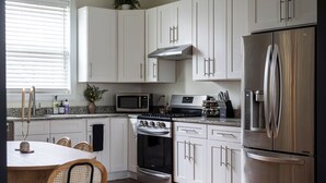 A modern kitchen with white cabinets, stainless steel appliances, a dining table with chairs, and a window with blinds. - 1 Mile to Downtown -Brewers Hill-Rooftop Deck-Gym (Milwaukee)