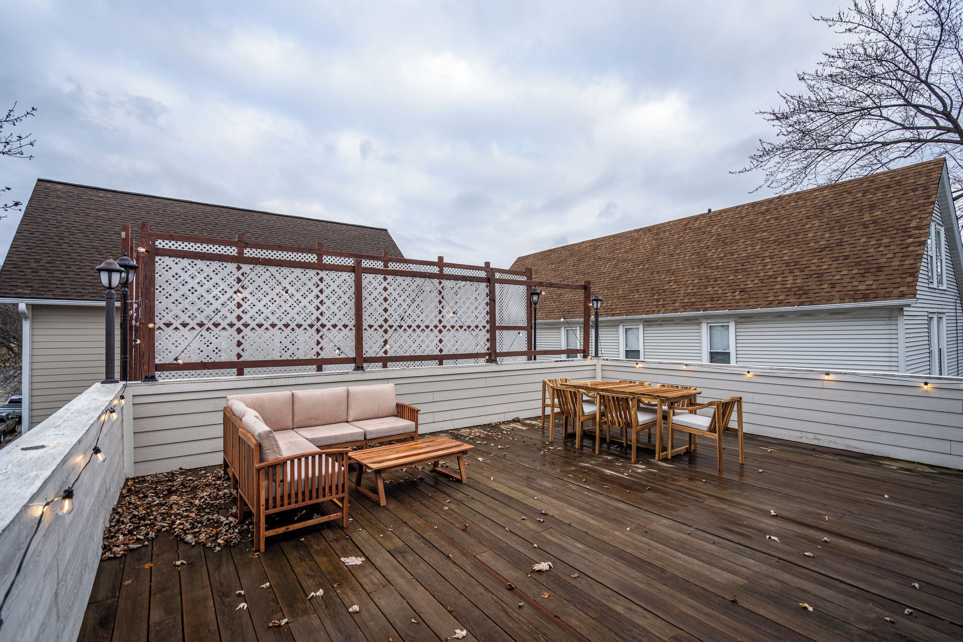 Een houten terras met een witte schutting, een bank en een tafel met stoelen.