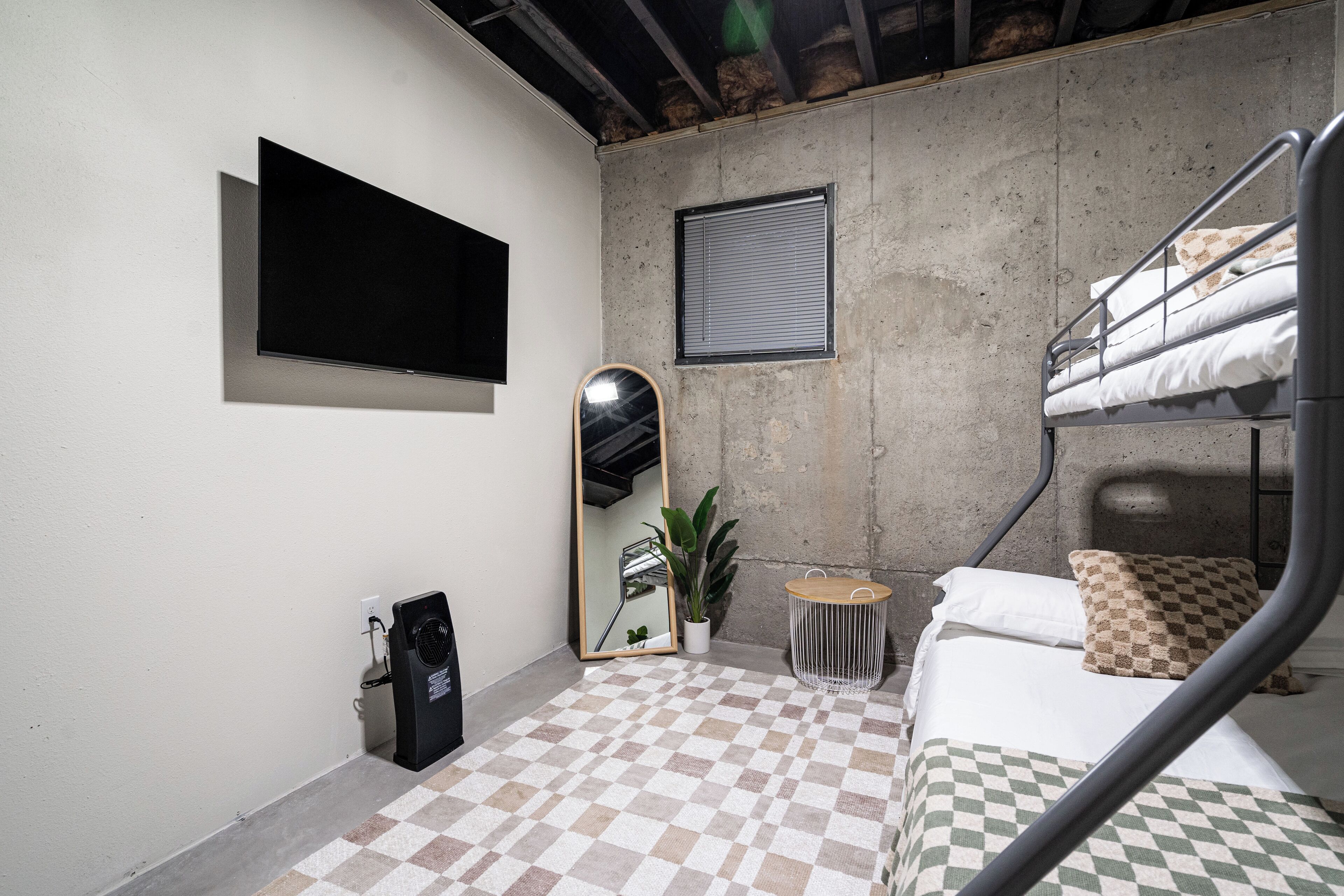 A small, compact room with a bunk bed, a flat-screen TV mounted on the wall, a small round table, and a potted plant.