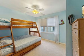 Une chambre avec un lit superposé, un ventilateur de plafond, une fenêtre avec des stores et une commode.