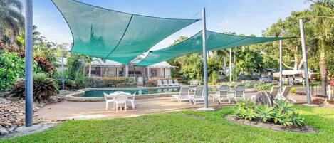 Un área de piscina con sillones reclinables y una zona de estar cubierta.