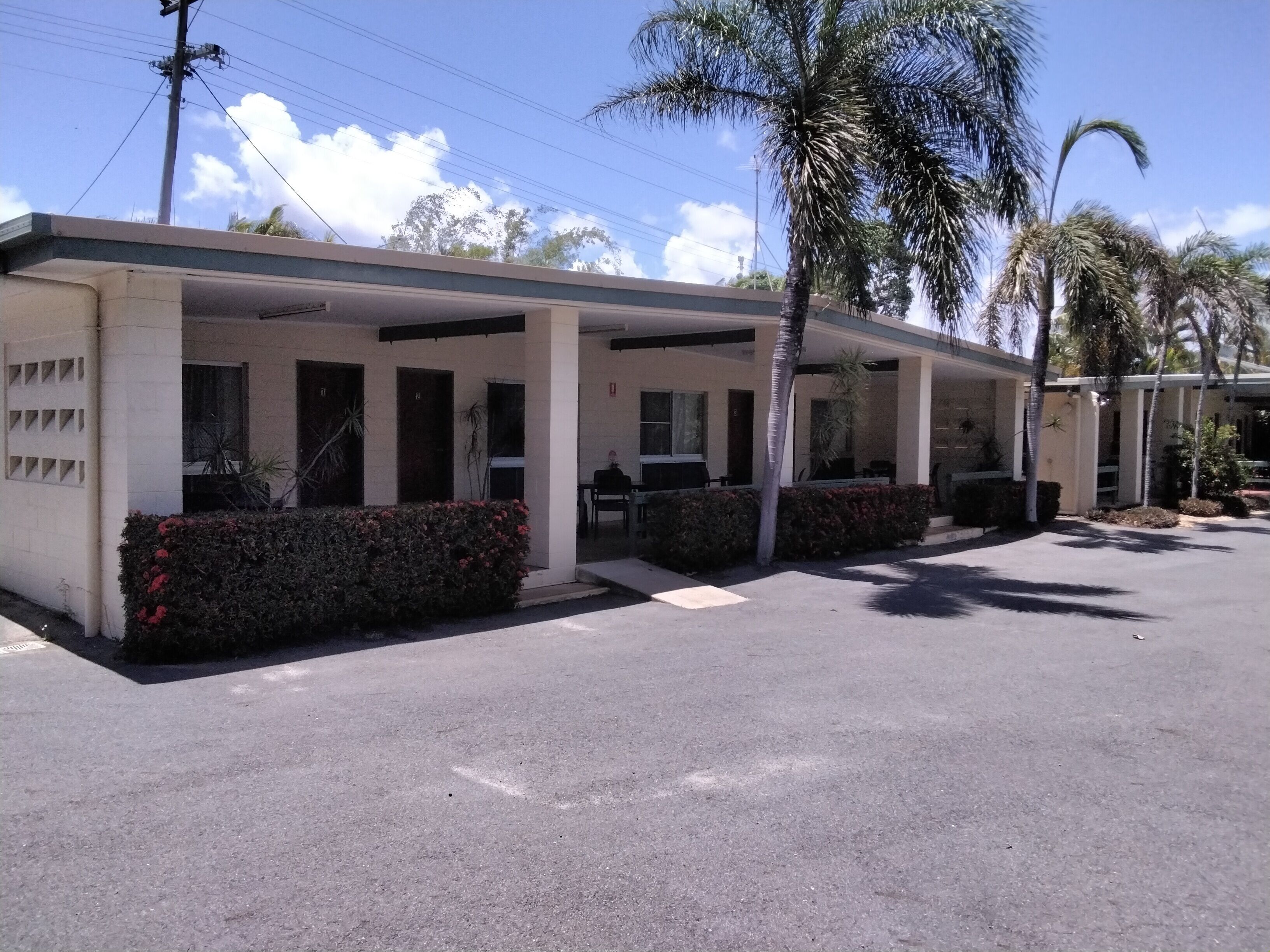 A motel with a covered parking area, palm trees, and a clear sky.