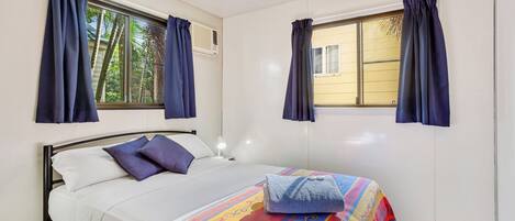 Una cama individual con una colcha colorida, dos almohadas y una mesita de noche con una lámpara.
