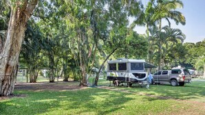 A camping area with a large RV and a pickup truck parked among trees. - COOKTOWN HOLIDAY PARK (Cooktown)