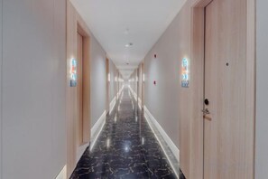 Un pasillo de hotel con piso de mármol, puertas de madera y luminarias fijadas a la pared.