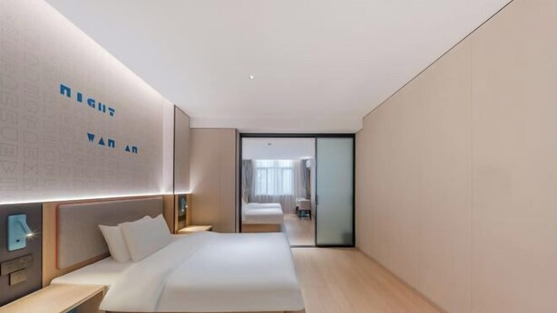 Een moderne hotelkamer met een groot bed, nachtkastjes en een muur met tekst.