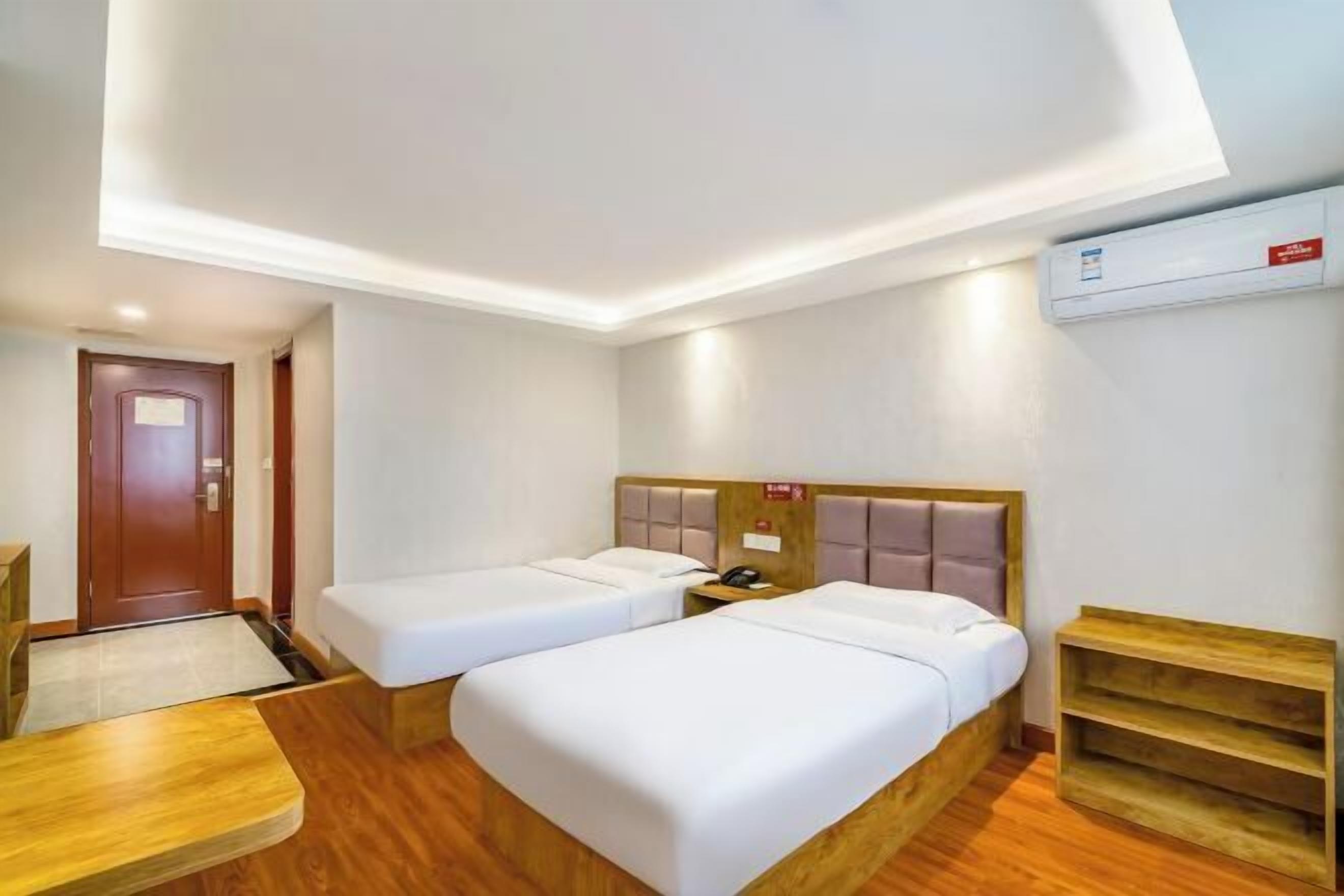 A hotel room with two single beds, a wooden desk, a small table, and a built-in shelf.