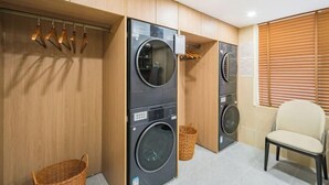 A laundry area with two stacked washing machines, wooden cabinets, a chair, and a basket. - Beijing ZhongKuang Hotel (Beijing)