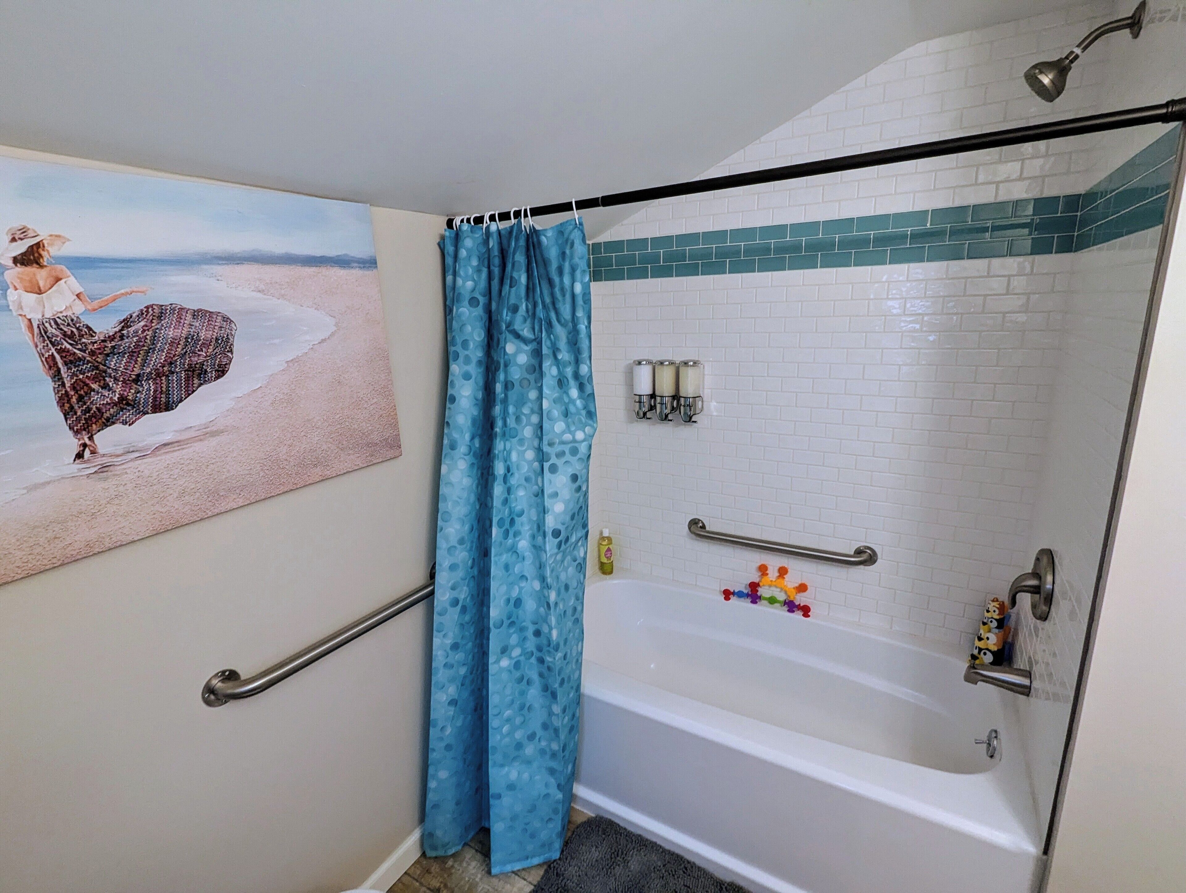 Une salle de bain équipée d’une douche, d’une baignoire, d’une barre d’appui, d’un porte-serviettes et de toilettes fixées au mur.