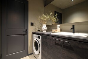 A modern kitchen with a built-in washer, dark cabinetry, and a vase with branches on the countertop. - Hotel Guild 5 (Tokyo)