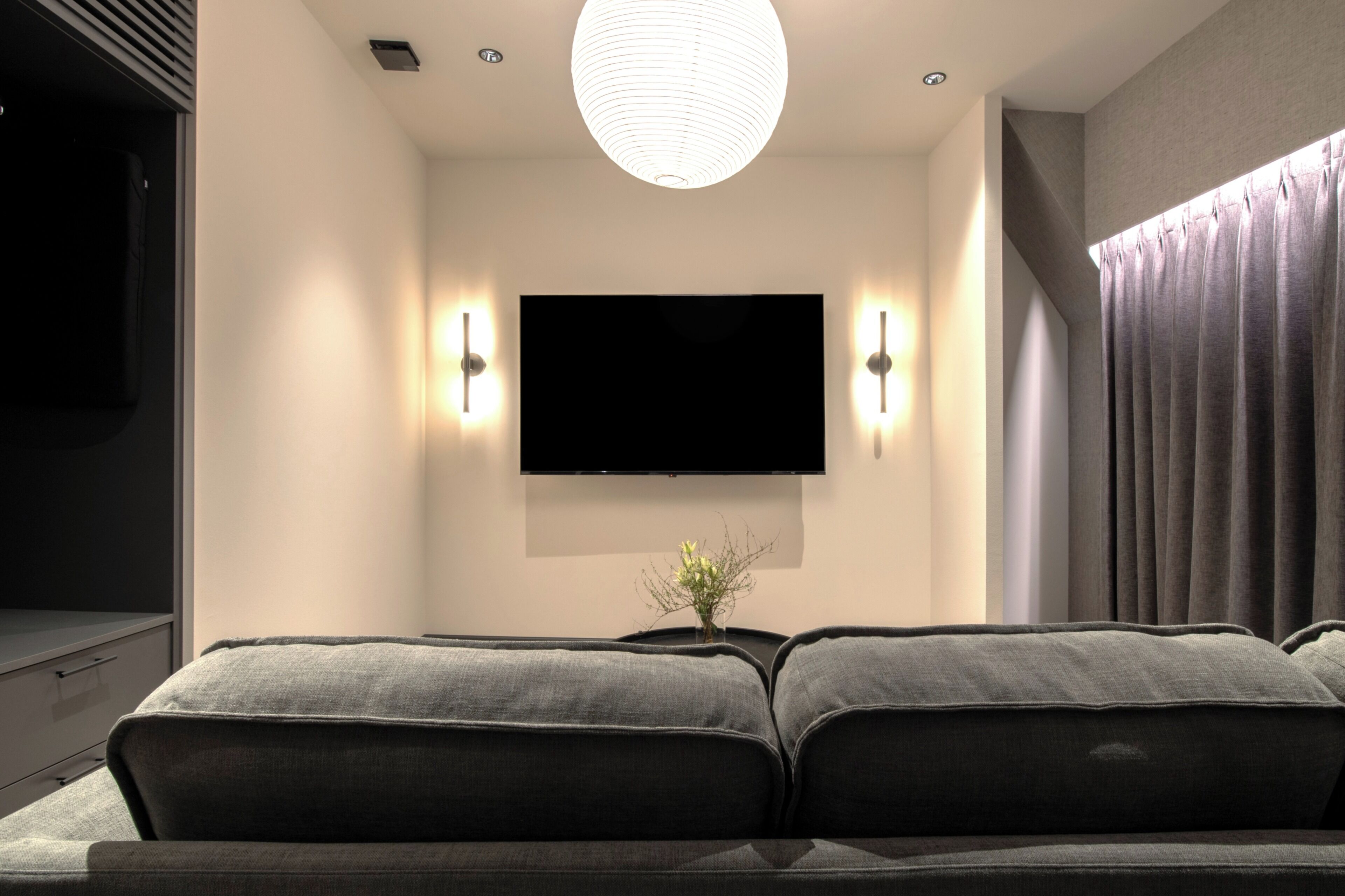 A modern living room with a flat-screen TV mounted on the wall, a sofa, and a pendant light.