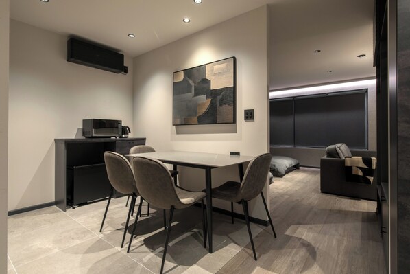 A modern kitchen with a microwave, a dining table with chairs, a sofa, and a large abstract painting on the wall.