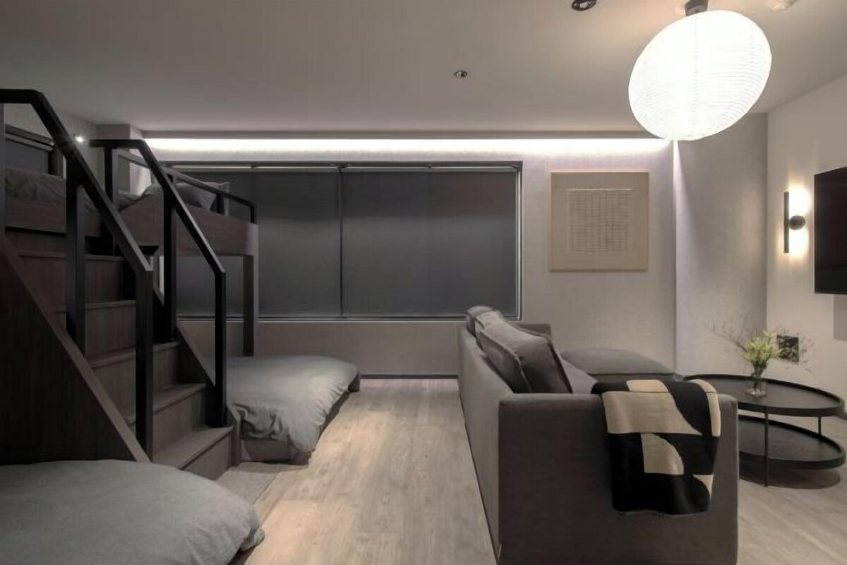 Une pièce moderne avec un escalier, un canapé, une petite table et un téléviseur fixé au mur.