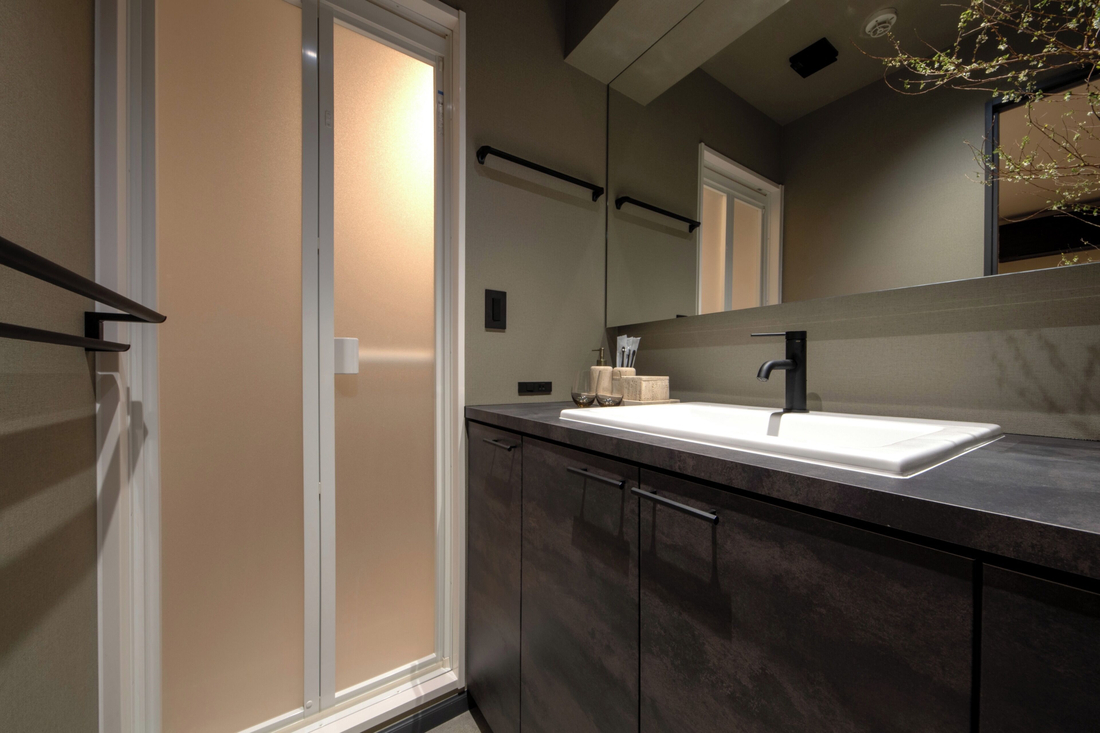 A modern bathroom with a large mirror, dark cabinetry, and a white sink.