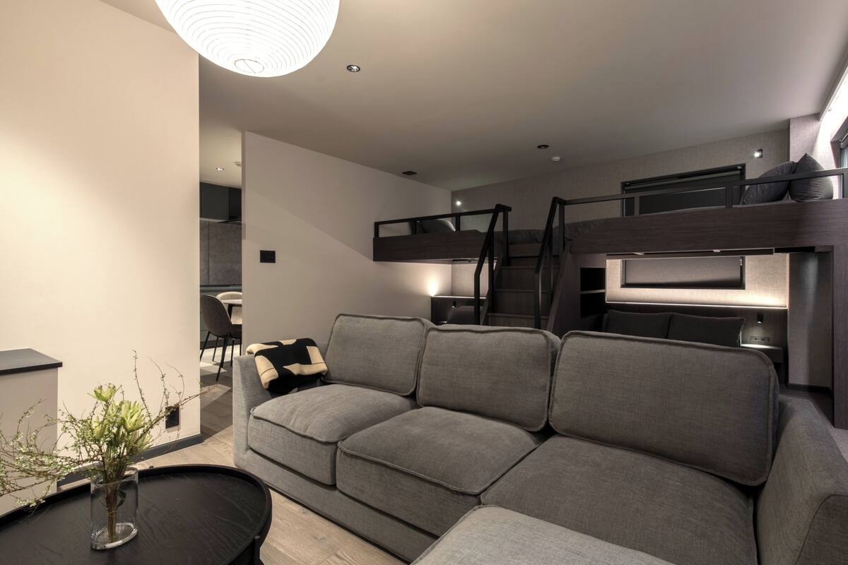 A modern living room with a grey sofa, a black coffee table, and a staircase leading to an upper level.