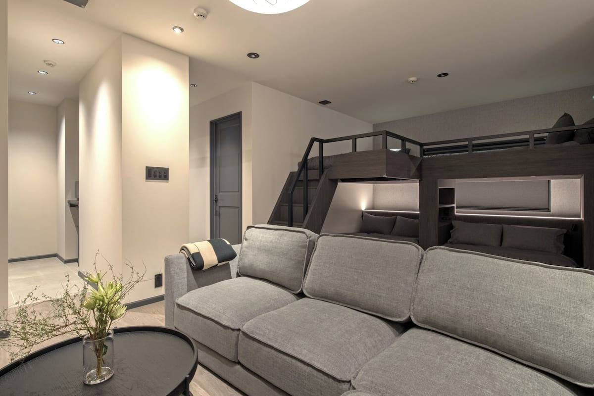 A modern living room with a sofa, a coffee table with a vase, a staircase, and a bed.