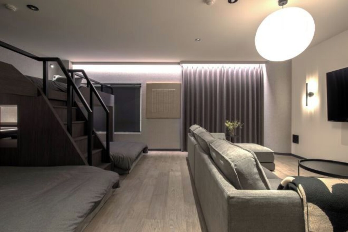 Une chambre moderne avec un lit superposé, un canapé, une petite table et un téléviseur fixé au mur.