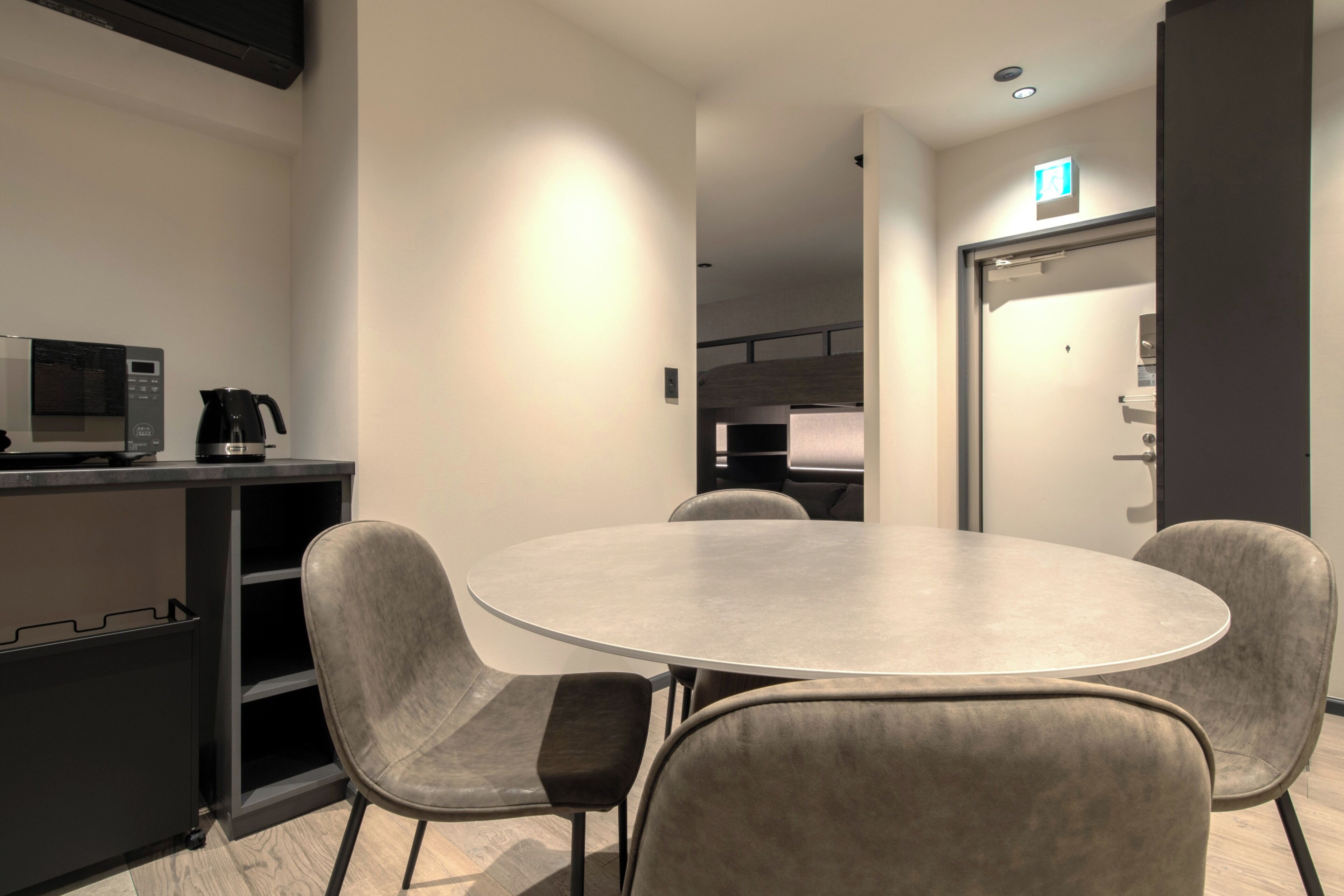A modern conference room with a round table, four grey chairs, a coffee machine, and a microwave.