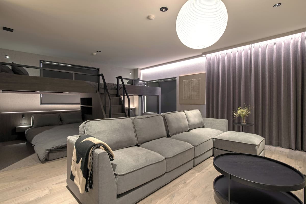 A modern living room with a sofa, a round table, a bunk bed, and a staircase.