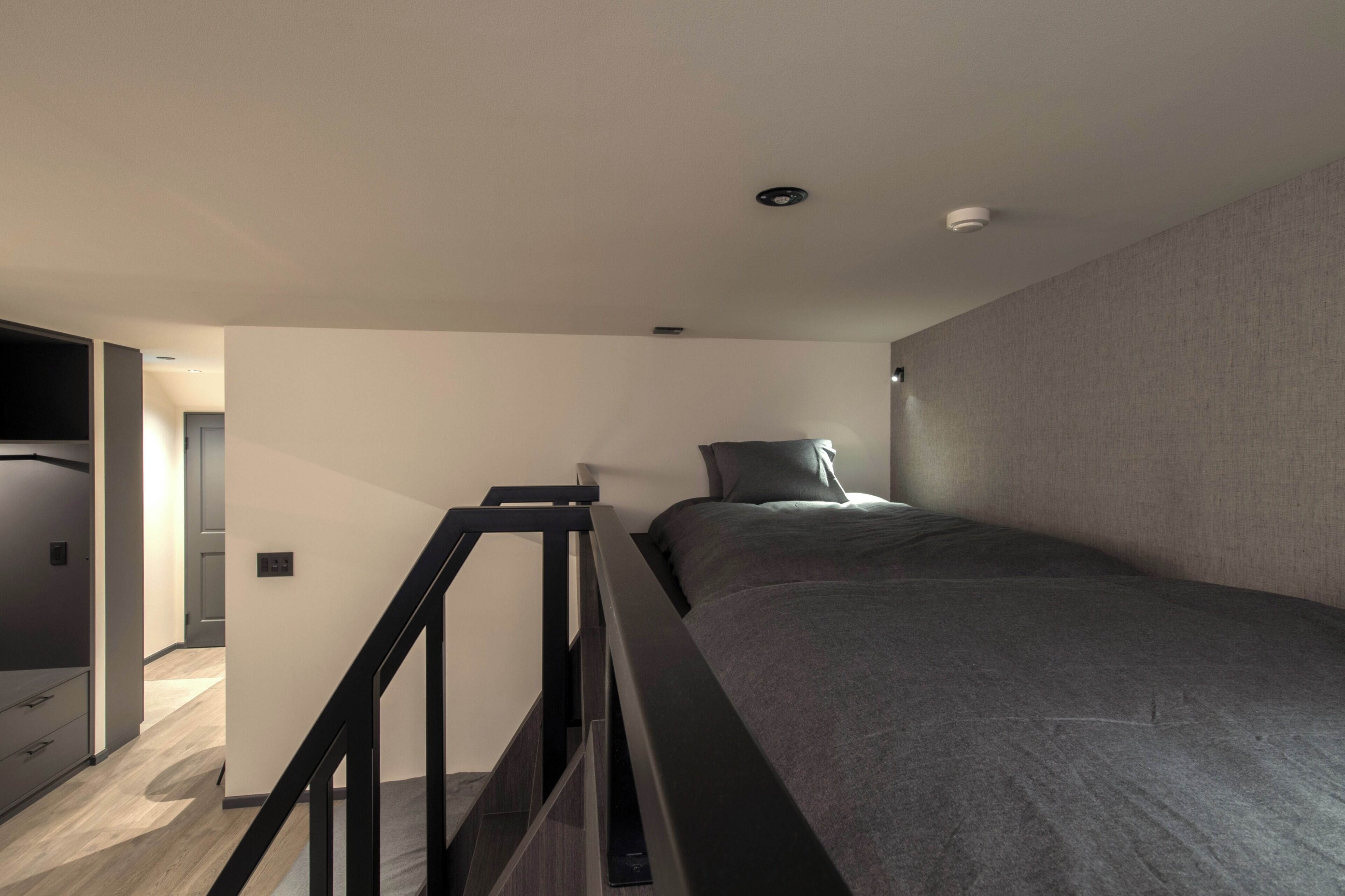 A modern bedroom with a bed, a staircase, and a hallway.