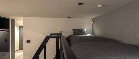 A modern bedroom with a bed, a staircase, and a hallway.
