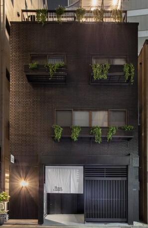 A modern building with a dark brick facade, multiple windows, and outdoor planters with greenery.