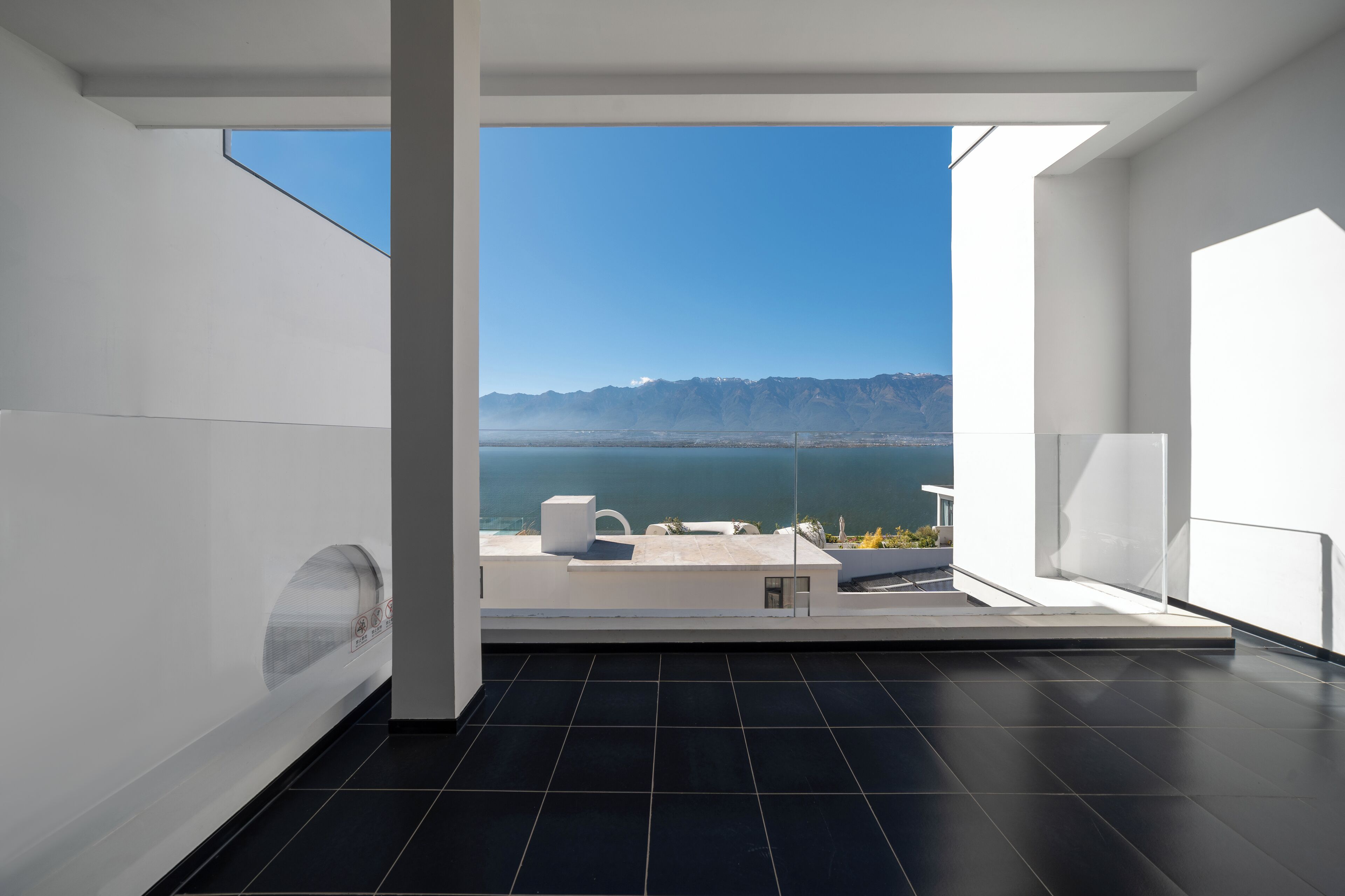 Una habitación moderna con un ventanal grande que ofrece vistas a un paisaje montañoso y una masa de agua.
