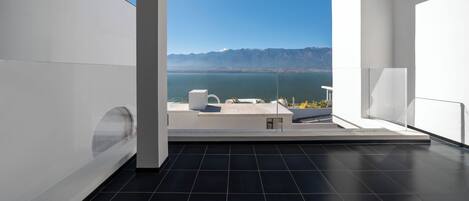 Una habitación moderna con un ventanal grande que ofrece vistas a un paisaje montañoso y una masa de agua.