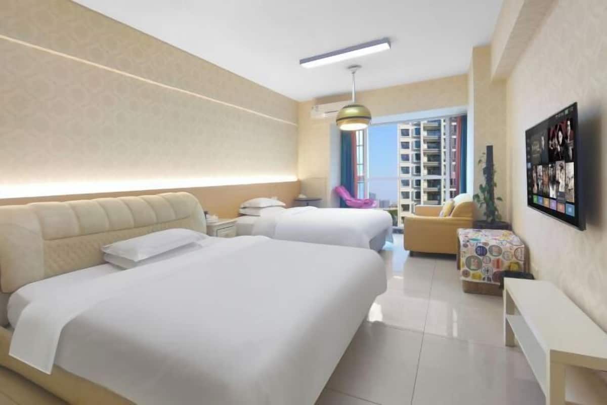 Ein Hotelzimmer mit zwei Betten, einem Sofa, einem kleinen Tisch, einem Fernseher und einem Balkon mit Blick auf Gebäude.