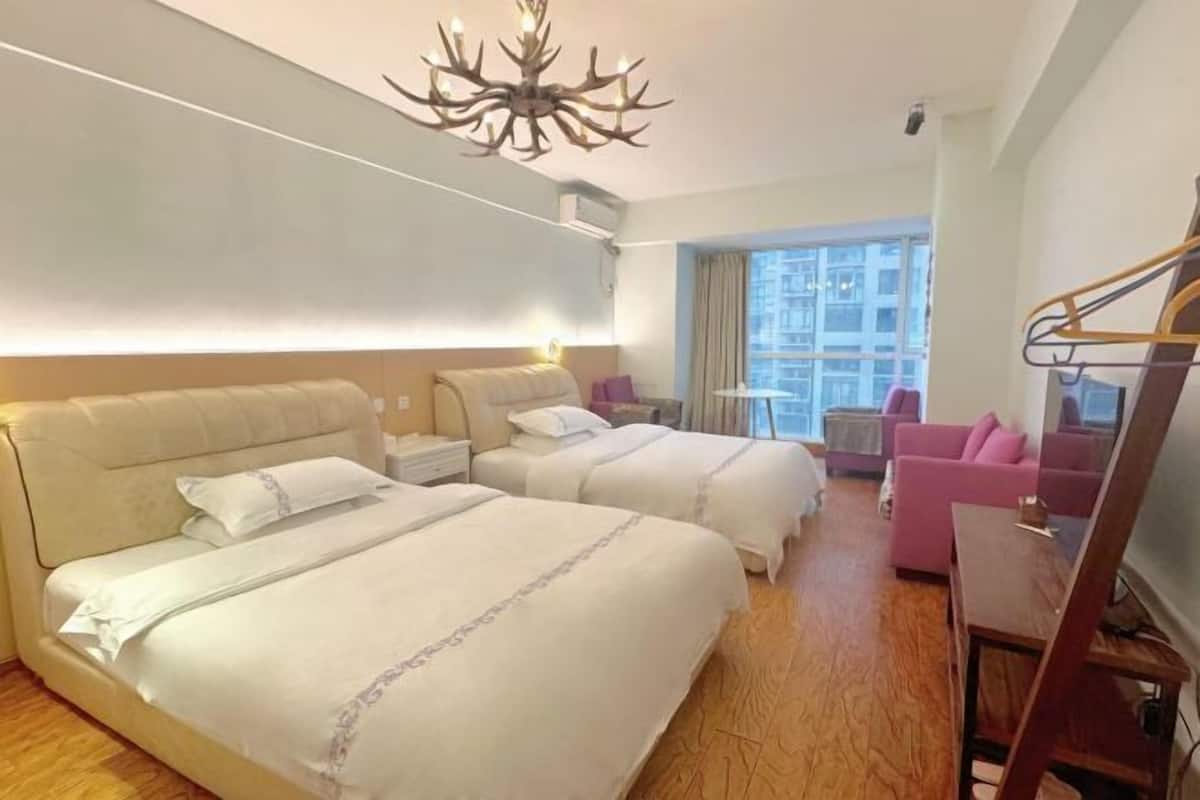 Ein Hotelzimmer mit zwei Betten, einer Couch, einem kleinen Tisch, einem Chandelier und Blick auf die Stadt.