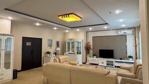 A modern living room with a beige sofa set, a flat-screen TV, and a white entertainment unit. - Bazhou Hotel (Urumqi)