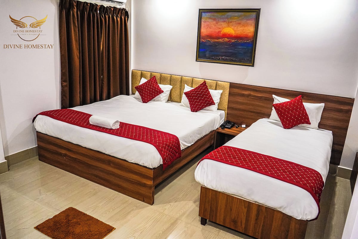A hotel room with two beds, each with white linens and red pillows, a wooden headboard, and a painting of a sunset on the wall.