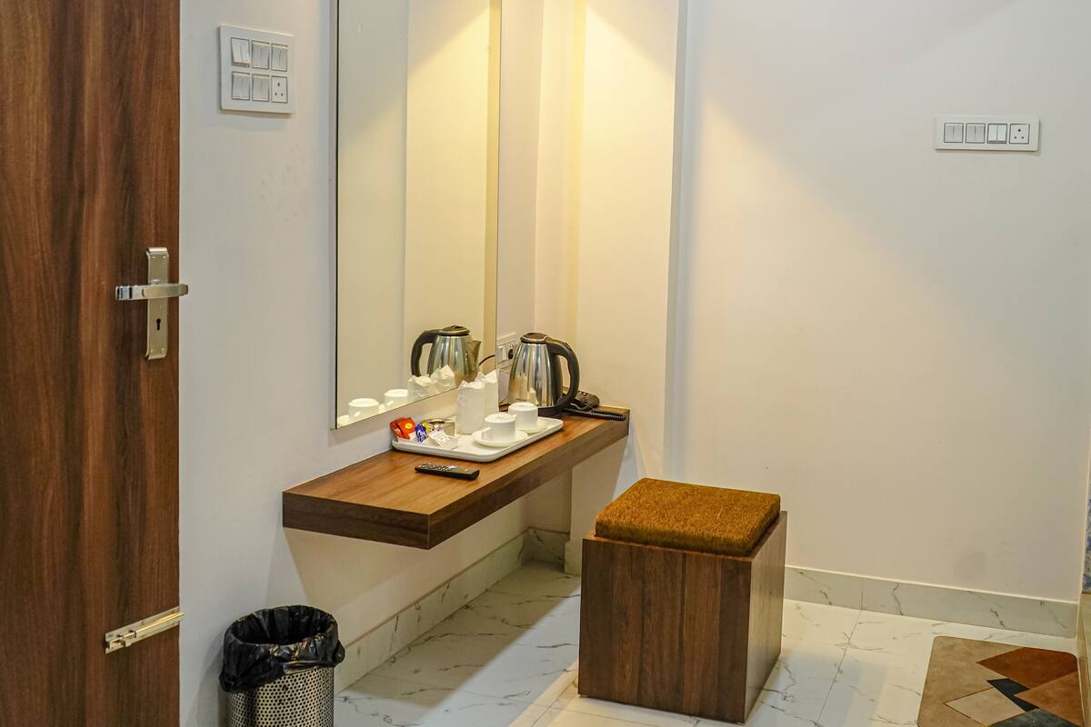 A bathroom with a wooden vanity, a mirror, a towel rack, a trash bin, and a small stool.