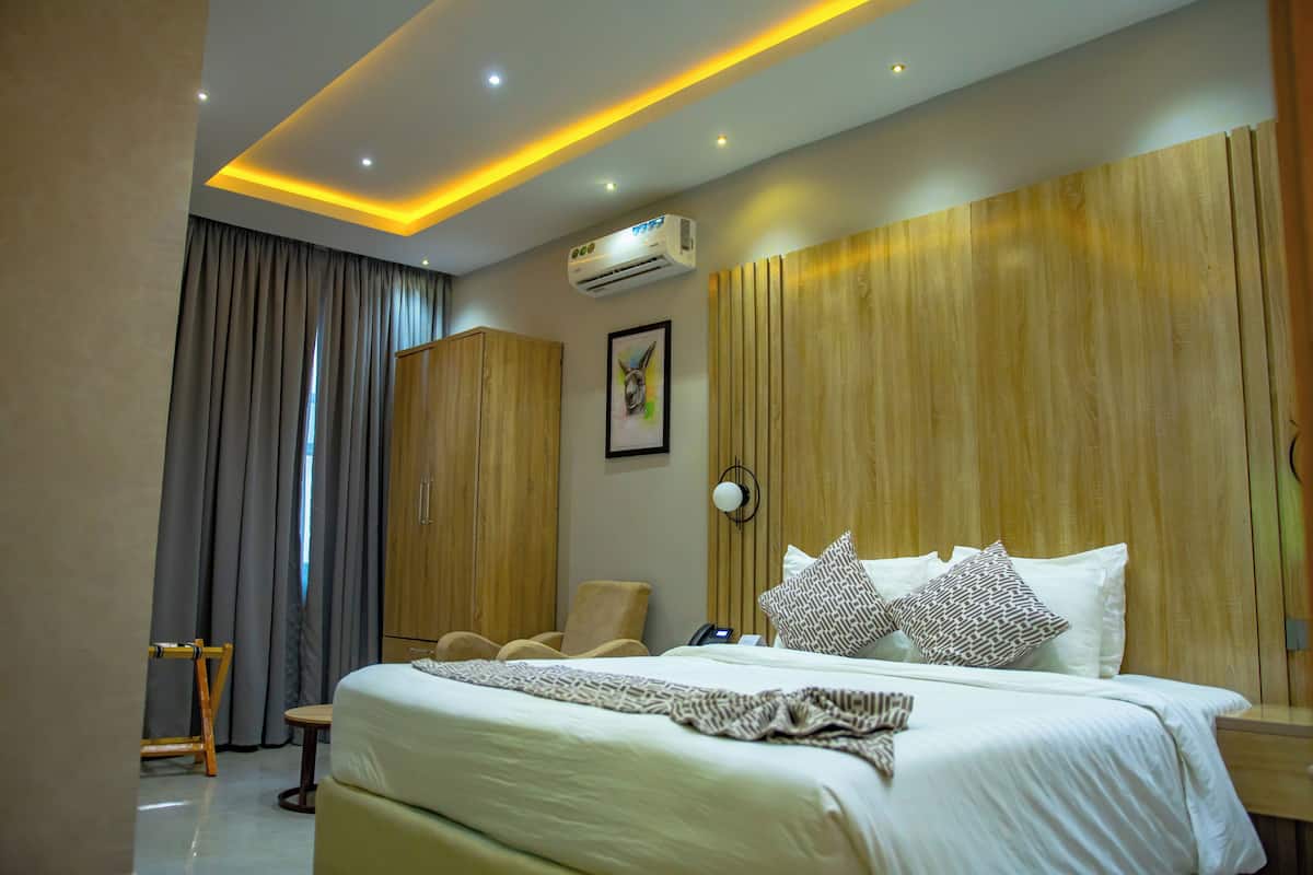 Ein Hotelzimmer mit einem großen Bett, einem Holzkopfstück, einem Schreibtisch mit Stuhl, einem Kleiderschrank und einer Klimaanlage.